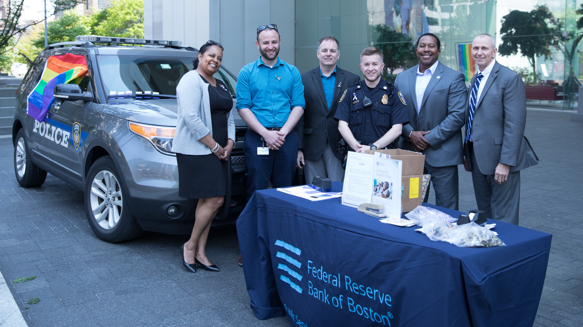 federal reserve bank of boston staff posing in front of the law enforcement cruiser with a pride flag long the side of it.